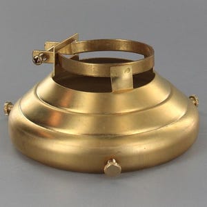 Peut inclure: Un support d'abat-jour de couleur laiton, avec un dessus circulaire et une base conique à rainures horizontales. Il comprend un support avec une vis pour fixer l'abat-jour. Le design est simple et fonctionnel.