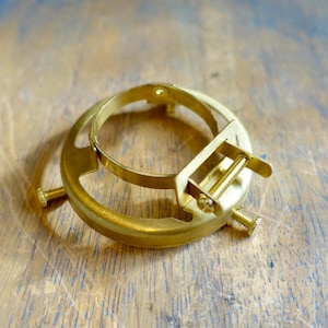 Peut inclure: Un support d'abat-jour de couleur laiton avec un design circulaire et une vis réglable. Le support a une forme d'anneau avec un anneau plus petit attaché et deux vis pour fixer l'abat-jour. Le matériel est conçu pour les lampes et les luminaires.
