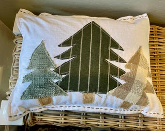 May include: Rectangular white pillow with three appliqued Christmas trees. The center tree is dark green with vertical stripes, flanked by a textured green tree and a tan plaid tree. The pillow has a stitched border.