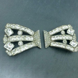 May include: A pair of vintage silver-tone shoe buckles with clear rhinestone embellishments. The buckles are shaped like a bow and have three rows of rhinestones.