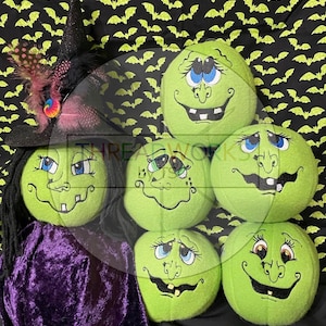 Könnte beinhalten: Eine Halloween-Dekoration mit grünen Plüsch-Hexengesichtern mit gestickten Merkmalen und verschiedenen Ausdrücken. Ein schwarzer Hexenhut mit Federn und ein violetter Samtumhang sind ebenfalls vorhanden. Der Hintergrund ist schwarz mit einem Muster aus gelben Fledermäusen.