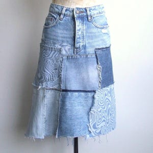Könnte beinhalten: Hellblauer Jeansrock mit Patchwork-Design. Der Rock weist verschiedene Blautöne auf, wobei einige Patches ein wellenförmiges Muster aufweisen. Der Rock hat ein klassisches Fünf-Taschen-Design und einen rohen Saum.