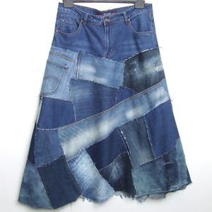 Op de afbeelding: Een spijkerbroekrok met een patchwork-ontwerp. De rok is gemaakt van verschillende tinten blauw denim, wat een unieke en textuurrijke uitstraling creëert. De rok hangt aan een hanger tegen een witte achtergrond.