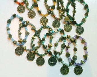 May include: Twelve zodiac sign charm bracelets with different colored beads and gold-toned spikes. Each bracelet features a different zodiac sign charm.