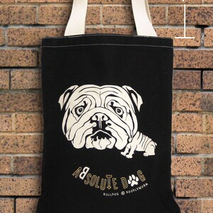 May include: Black tote bag with a cream-colored bulldog graphic and cream-colored handles. The bag is approximately 7 inches in height. The text "ABSOLUTE DOG" and "BULLDOG @ POODLEWORM" is printed on the bag.