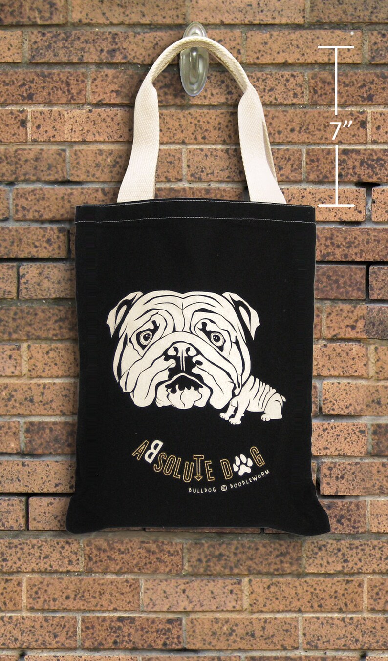 May include: Black tote bag with a cream-colored bulldog graphic and cream-colored handles. The bag is approximately 7 inches in height. The text "ABSOLUTE DOG" and "BULLDOG @ POODLEWORM" is printed on the bag.