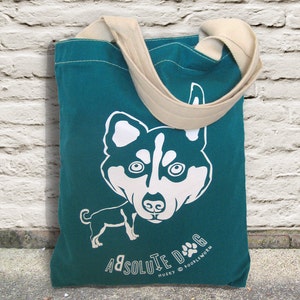 May include: Teal tote bag with a white graphic of a Husky dog. The bag has a beige strap and the words "Absolute Dog" and "Husky" printed on it. The bag is made of canvas and is suitable for carrying groceries or other items.