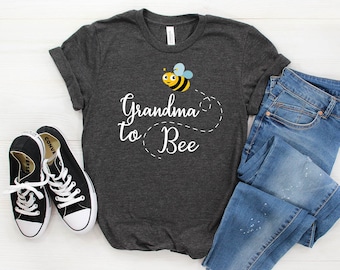 May include: A dark gray t-shirt with a white graphic of a bee and the text "Grandma to Bee".