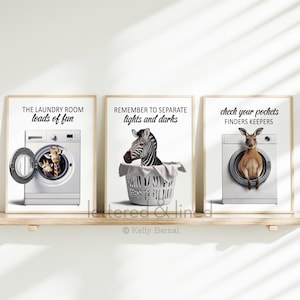 May include: Three framed prints with animal illustrations and laundry-themed text. The first print features a giraffe and baby giraffe in a washing machine with the text "The Laundry Room loads of fun". The second print features a zebra in a laundry basket with the text "Remember to separate lights and darks". The third print features a kangaroo in a washing machine with the text "Check your pockets Finders Keepers".