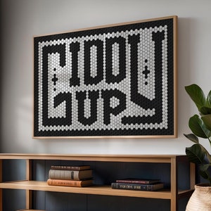 May include: A wooden shelf unit with two shelves, featuring a black and white mosaic tile art piece with the word "PLAY" in a stylized font. The shelf unit is against a dark grey wall and has books on the shelves.