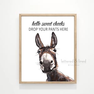 May include: A printable wall art design featuring a cartoon donkey with the text "hello sweet cheeks drop your pants here" and the signature "lettered & lined Kelly  Designs".