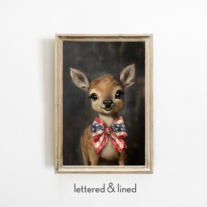 Puede incluir: Pintura enmarcada de un cervatillo con una pajarita con los colores de la bandera estadounidense. La obra de arte tiene un marco de madera clara y un fondo oscuro. El texto "lettered & lined" est&aacute; en la parte inferior de la imagen. El cervatillo tiene ojos grandes.