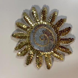 Può includere: Un sole di paillettes dorate e argentate con un design a spirale al centro.
