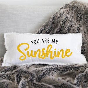 Könnte beinhalten: Ein weißes Kissen mit ausgefransten Kanten und dem Text "You are my Sunshine" in schwarzer und gelber Schrift.