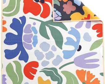 Könnte beinhalten: Ein rechteckiges Küchentuch mit weißem Hintergrund und einem bunten Blumenmuster in Rot, Orange, Gelb, Hellblau, Dunkelblau, Lavendel und Grün. Das Tuch hat eine Waffelstruktur, einen hellbeigen Rand und ein kleines weißes Etikett mit der Aufschrift WILDWOOD.