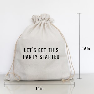 Könnte beinhalten: Ein beigefarbener Kordelzugbeutel mit dem Text "LET'S GET THIS PARTY STARTED" in Schwarz. Die Tasche ist 35,5 cm breit und 40,6 cm hoch. Die Tasche ist aus einem Naturstoff gefertigt.