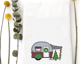 Puede incluir: Toalla de mano blanca con un diseño bordado de una caravana vintage decorada para Navidad. La caravana es roja, azul y verde, con un árbol de Navidad y luces de cadena. Flores amarillas y follaje verde.