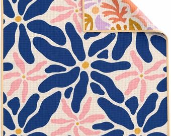 Könnte beinhalten: Ein rechteckiges Waffelpiqué-Küchentuch mit einem sich wiederholenden Blumenmuster in Marineblau, Hellrosa und Gelb auf cremeweißem Grund. Die obere Ecke ist umgeschlagen und zeigt ein sekundäres Muster aus abstrakten Formen in Lavendel, Orange und Gold.