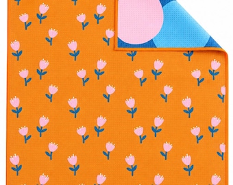 Könnte beinhalten: Ein rechteckiges Küchentuch mit orangefarbenem Hintergrund und einem wiederkehrenden Muster aus kleinen rosa Tulpen mit blauen Stielen. Die obere rechte Ecke ist umgeschlagen und zeigt eine blaue Rückseite mit großen rosa und hellblauen Kreisen.