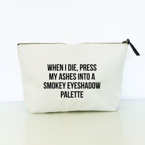 May include: White canvas makeup bag with a black zipper and a black pull tab. The bag has the text "WHEN I DIE, PRESS MY ASHES INTO A SMOKEY EYESHADOW PALETTE" printed on it.