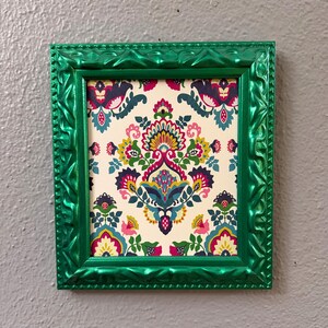 May include: A rectangular picture frame with a metallic emerald green finish and a textured, scalloped border. The frame contains a print featuring a repeating damask-style pattern in vibrant shades of magenta, teal, yellow, and dark blue on a cream background.