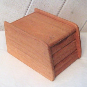 May include: A wooden bread box with three drawers. The box is light brown and has a curved front.