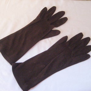 May include: A pair of brown long gloves made of a soft fabric. The gloves are laying flat on a white surface.
