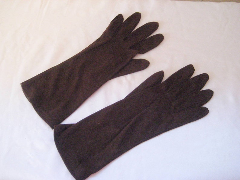 May include: A pair of brown long gloves made of a soft fabric. The gloves are laying flat on a white surface.
