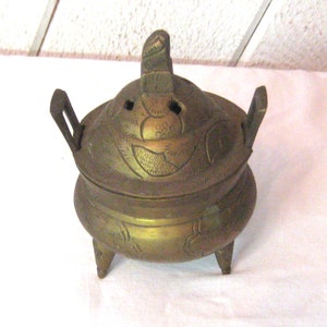 May include: A brass incense burner with a lid and three legs. The burner is decorated with floral designs.