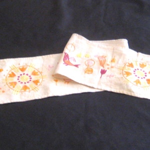 May include: A white fabric runner with embroidered birds, flowers, and geometric designs in shades of orange, yellow, and red.