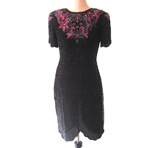 May include: A black sequined dress with a pink and purple floral design on the neckline. The dress has short sleeves and a fitted silhouette.