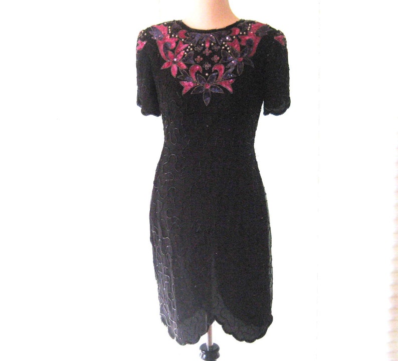 May include: A black sequined dress with a pink and purple floral design on the neckline. The dress has short sleeves and a fitted silhouette.