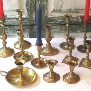 Puede incluir: Una colección de candelabros de latón de varios tamaños y diseños, algunos con velas rojas y azules. Los candelabros tienen diferentes bases, incluyendo formas redondas, cuadradas y hexagonales. La estética general es vintage y decorativa.