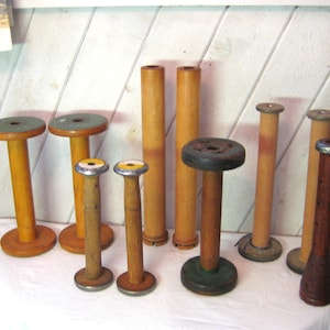 Könnte beinhalten: Eine Sammlung von Vintage-Holzspulen und -spulen in verschiedenen Größen und Farben. Die Spulen haben eine zylindrische Form mit einem zentralen Loch, die Spulen haben ein konisches Design. Einige Spulen haben einen grünen oder blauen Deckel.