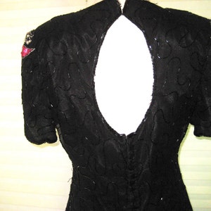 May include: A black sequined dress with a low back and short sleeves. The dress has red and silver embellishments on the shoulders.