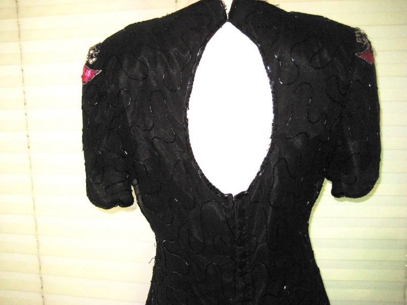 May include: A black sequined dress with a low back and short sleeves. The dress has red and silver embellishments on the shoulders.