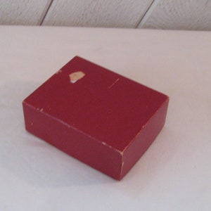 May include: A red cardboard box with a small white mark on the top.