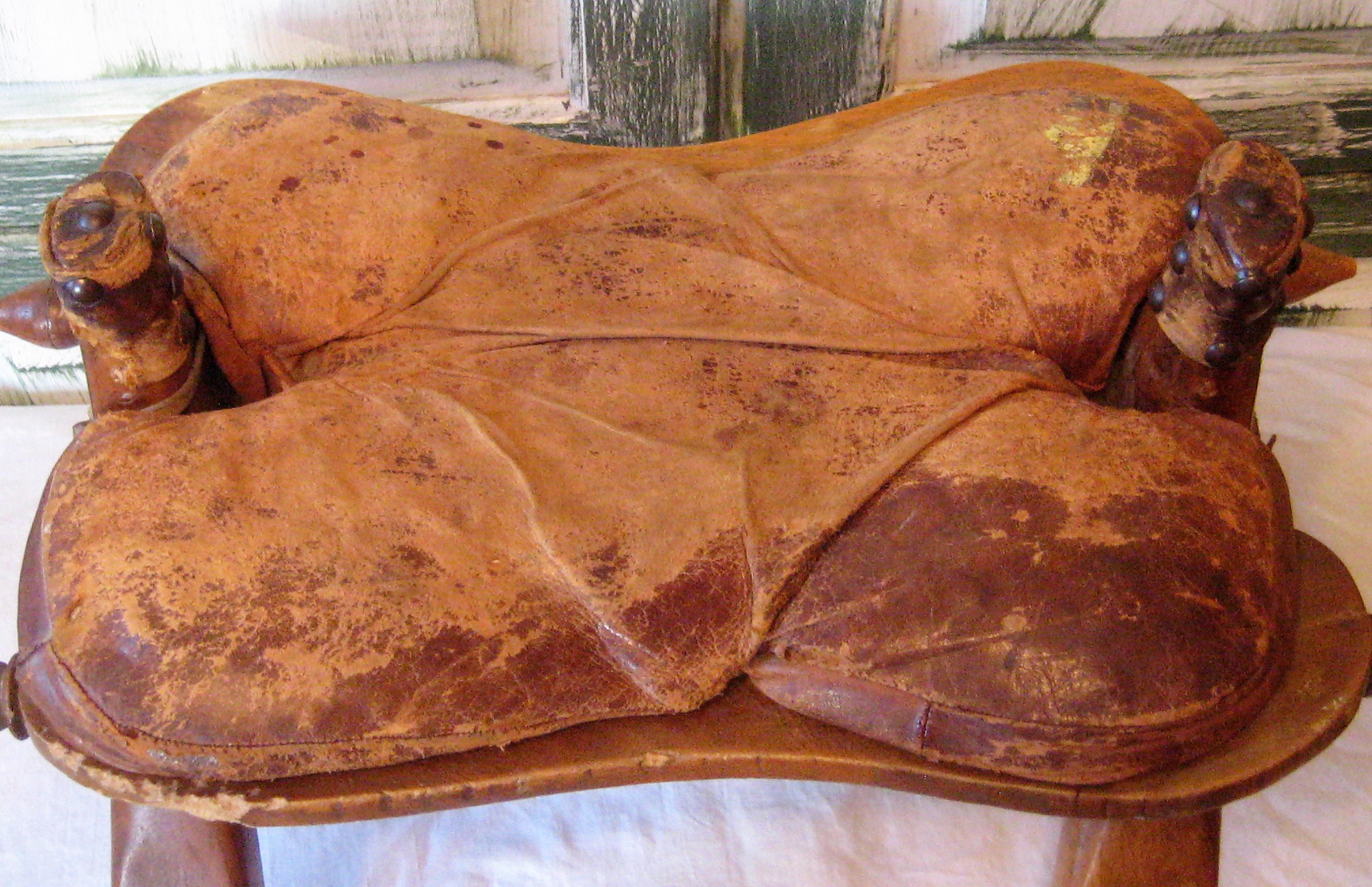 アンティークのラクダの鞍、素朴な木製の足置き、古びた素朴な布張りの