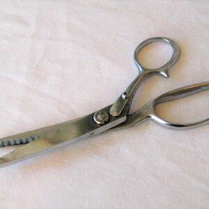 May include: Silver-toned fabric shears with a serrated blade and a classic design. The shears have a comfortable grip and are ideal for cutting fabric.