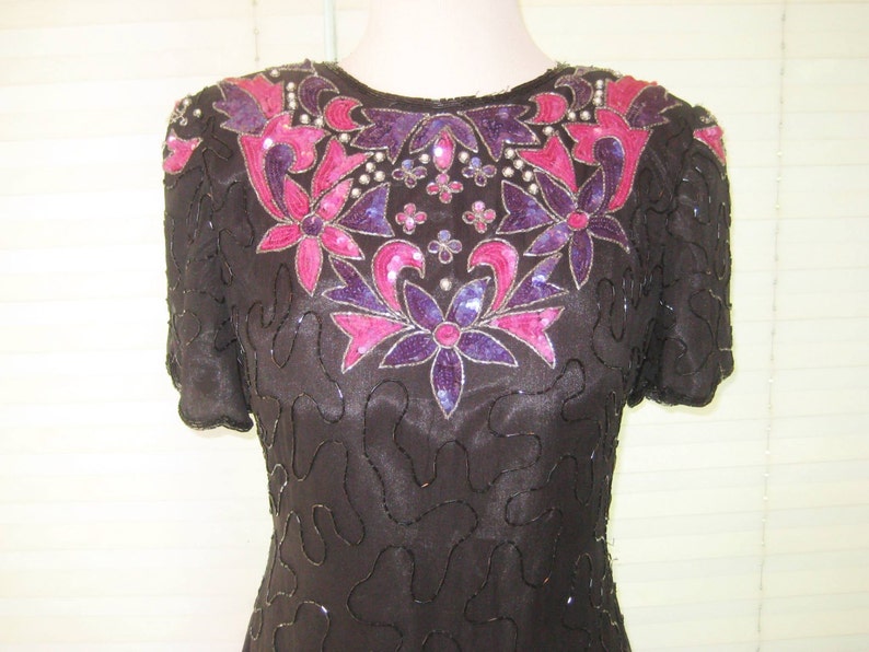 May include: A black sequined dress with a floral design in shades of pink and purple. The dress has short sleeves and a scoop neckline.