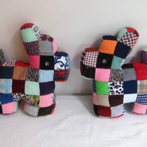 Puede incluir: Dos juguetes para perros de tela patchwork. Los perros están hechos de varios colores y patrones de tela, incluyendo rosa, verde, azul, rojo y marrón. Los perros tienen ojos de botón y están cosidos juntos con una puntada simple.