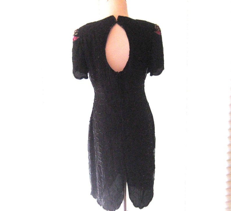 May include: A black sequined dress with a keyhole back and short sleeves. The dress has red and gold embellishments on the shoulders.