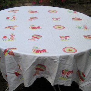May include: White tablecloth with a colorful Mexican-themed pattern. The pattern includes sombreros, donkeys, and other festive designs.