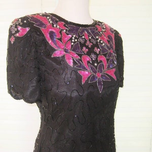 May include: A black sequined dress with a pink and purple floral design. The dress has short sleeves and a round neckline.