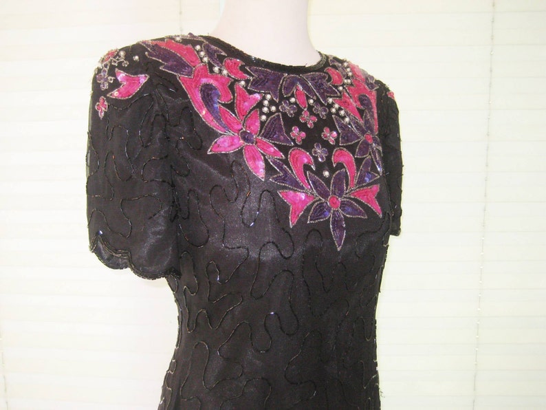 May include: A black sequined dress with a pink and purple floral design. The dress has short sleeves and a round neckline.