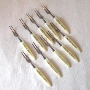 May include: Set of ten silver cake forks with white handles decorated with gold floral designs.
