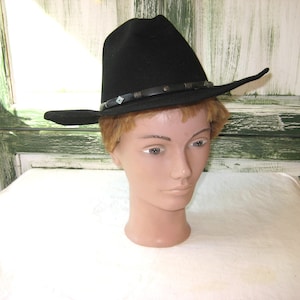 Pode incluir: Um chapéu de cowboy de feltro preto com uma faixa de couro preta e detalhes prateados.