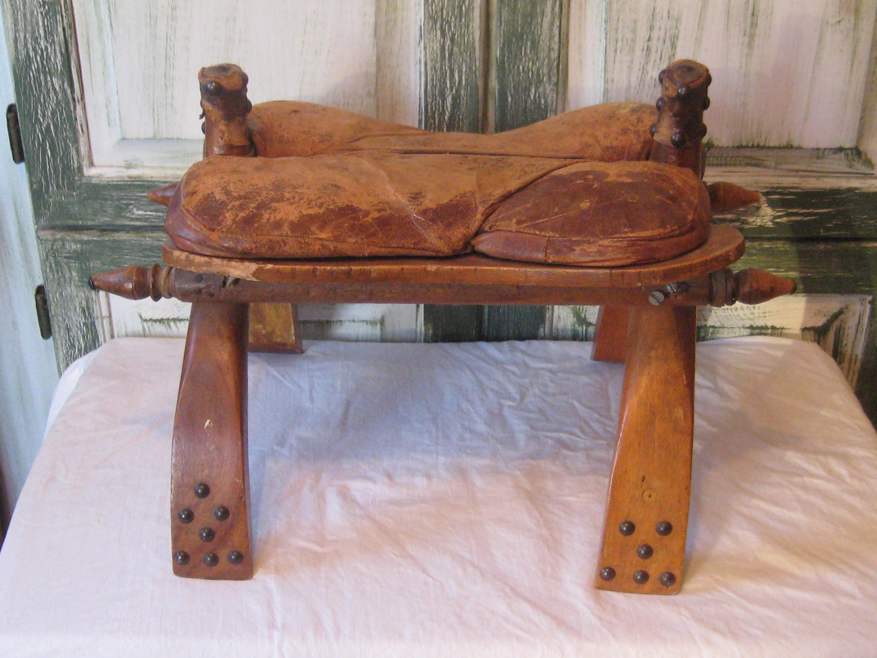 アンティークのラクダの鞍、素朴な木製の足置き、古びた素朴な布張りの