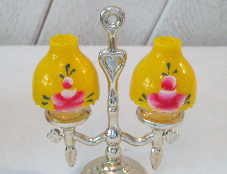 May include: A silver two-light lamp with yellow glass lampshades painted with pink roses and green leaves.