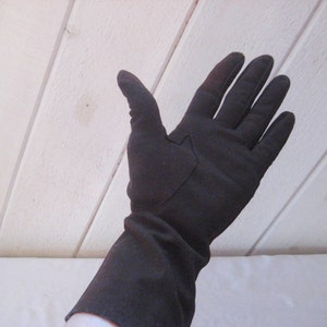 May include: A pair of long black gloves made of a soft fabric. The gloves have a seam down the back of the hand and a small patch on the back of the hand.